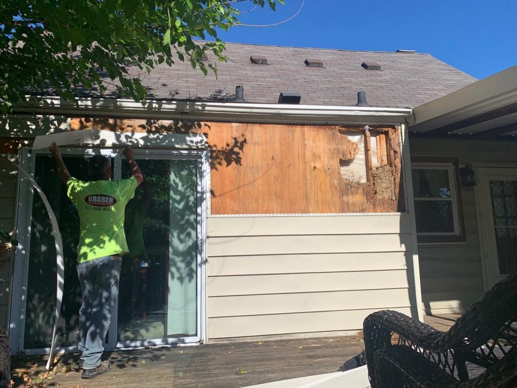 A house with its old siding removed, showing bare wood sheathing, with new vinyl siding partly installed