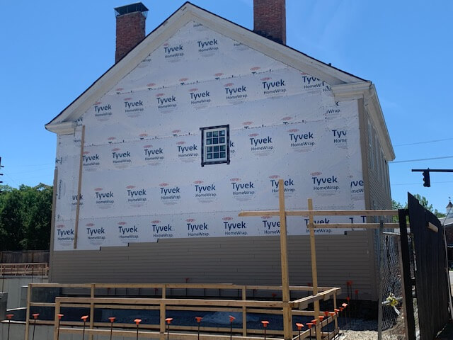 A two-story house wrapped in house wrap, with scaffolding along the wall, before new siding goes on